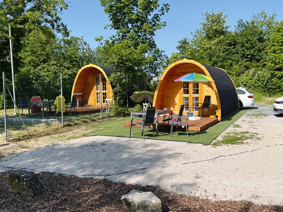 Zwei Campingpods von aussen, jeder mit eigener Holzterrasse und Sitzgruppe