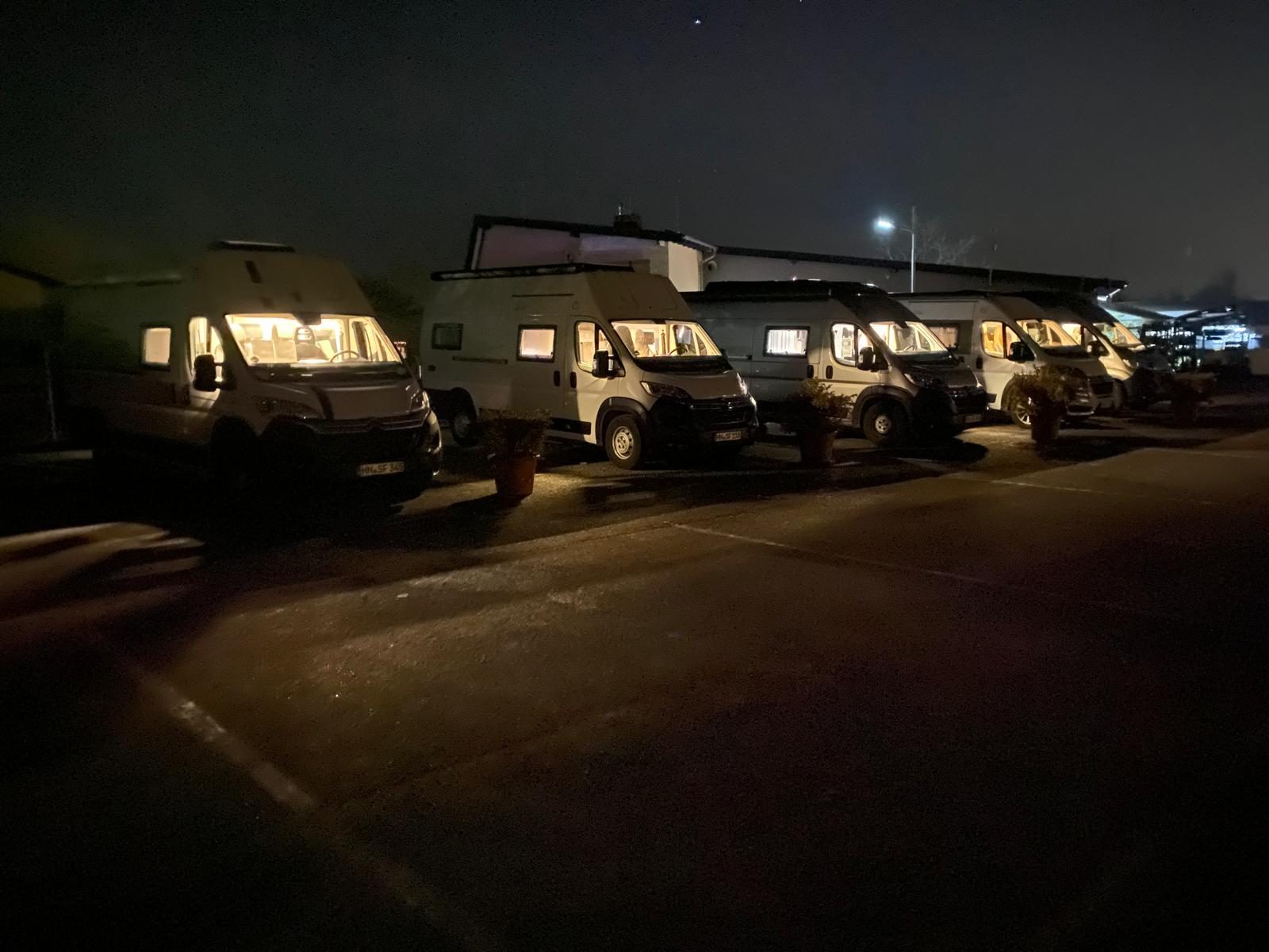 Reisemobile am Abend nebeneinander auf dem Platz, die Fenster warm beleuchtet