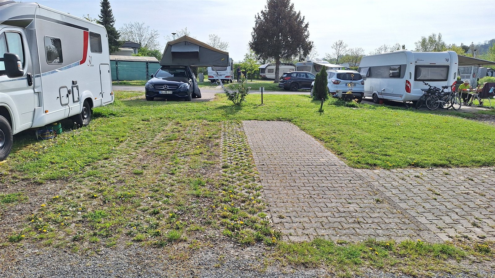 Ferien-Stellplätze auf dem Platz: Wohnwagen, Reisemobil und Auto mit Dachzelt auf parzellierten Plätzen mit befestigter Fahrspur
