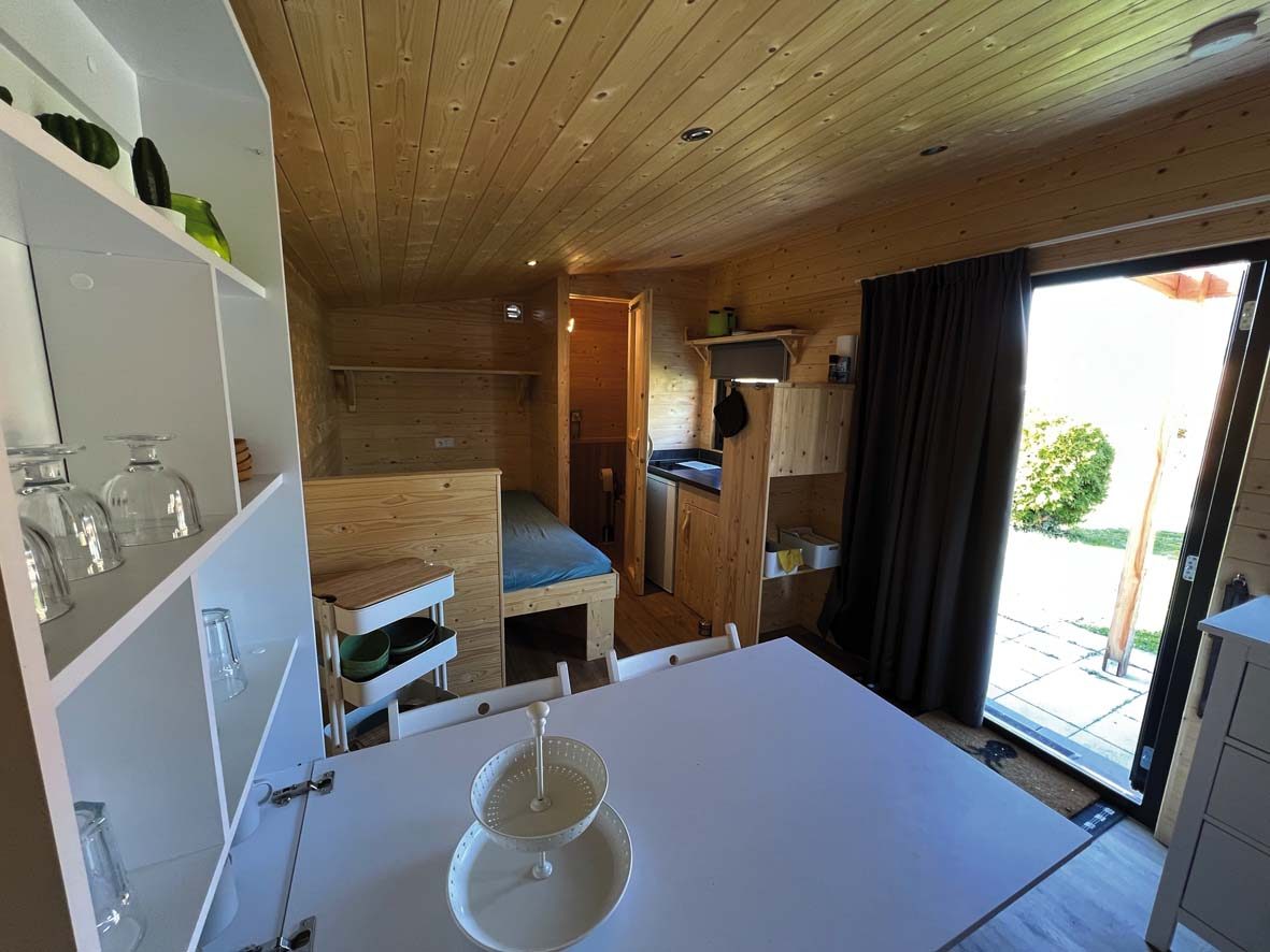 Woodlodge von innen: Küchenzeile, Esstisch und Stockbett unter Holzdecke