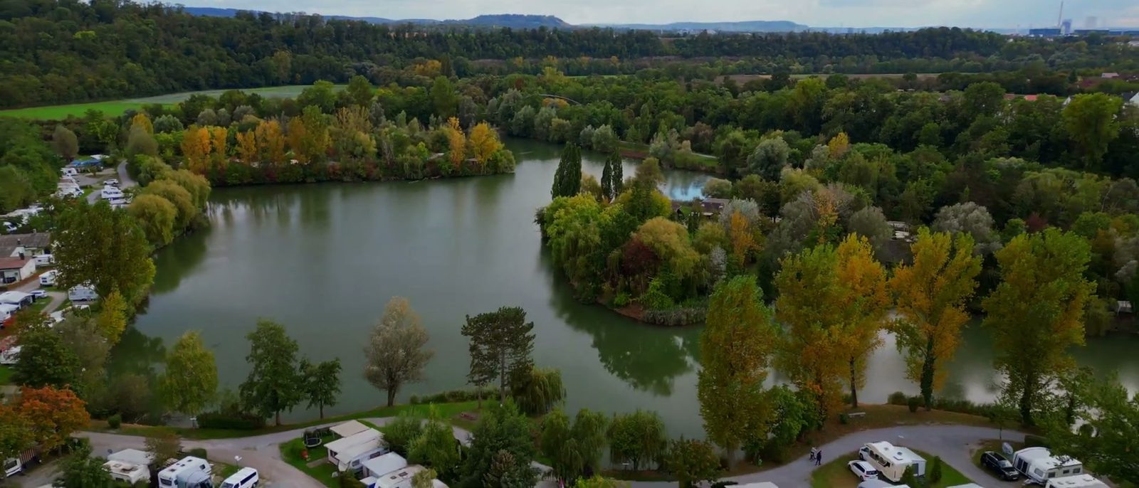 Luftaufnahme des Sperrfechter Freizeitparks: der Hirschfeldsee mit Insel, davor die Stellplatzreihen mit Wohnwagen und Wohnmobilen